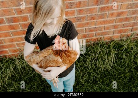 Junge blonde Mädchen hält ihr Haustier Huhn Blick auf die Hähnchen Stockfoto