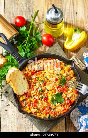 Traditionelles türkisches Gericht. Mememen (gebratenes Gemüse mit Rührei) in einer gusseisernen Pfanne auf einem Holztisch. Stockfoto