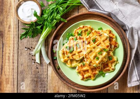 Nicht süße Waffeln mit Kartoffeln, Erbsen, Paprika, Käse werden mit Sauerrahm und Kräutern auf einem Teller auf einem rustikalen Tisch serviert. Draufsicht flach liegend. Kopieren Stockfoto