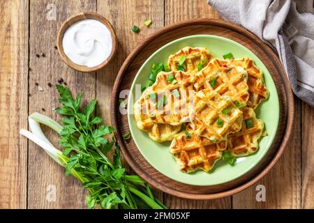 Nicht süße Waffeln mit Kartoffeln, Erbsen, Paprika, Käse werden mit Sauerrahm und Kräutern auf einem Teller auf einem rustikalen Tisch serviert. Draufsicht flach liegend. Stockfoto