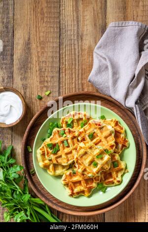 Nicht süße Waffeln mit Kartoffeln, Erbsen, Paprika, Käse werden mit Sauerrahm und Kräutern auf einem Teller auf einem rustikalen Tisch serviert. Draufsicht flach liegend. Kopieren Stockfoto