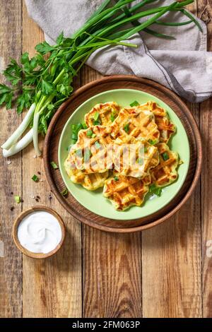 Nicht süße Waffeln mit Kartoffeln, Erbsen, Paprika, Käse werden mit Sauerrahm und Kräutern auf einem Teller auf einem rustikalen Tisch serviert. Draufsicht flach liegend. Kopieren Stockfoto