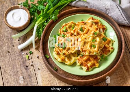 Nicht süße Waffeln mit Kartoffeln, Erbsen, Paprika, Käse werden mit Sauerrahm und Kräutern auf einem Teller auf einem rustikalen Tisch serviert. Speicherplatz kopieren. Stockfoto