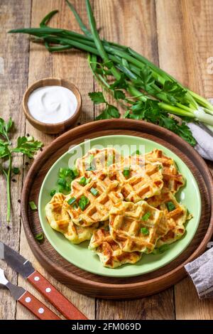 Nicht süße Waffeln mit Kartoffeln, Erbsen, Paprika, Käse werden mit Sauerrahm und Kräutern auf einem Teller auf einem rustikalen Tisch serviert. Stockfoto