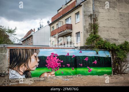 Ein Graffiti an einer alten Mauer zeigt ein Mädchen, welches wie bei einer Pusteblume ein Coronavirus anpustet, welches dann auseinander fliegt. Ein s Stockfoto