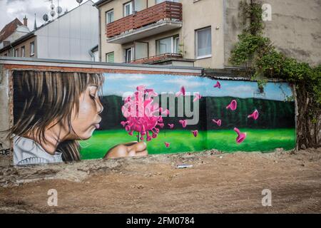 Ein Graffiti an einer alten Mauer zeigt ein Mädchen, welches wie bei einer Pusteblume ein Coronavirus anpustet, welches dann auseinander fliegt. Ein s Stockfoto