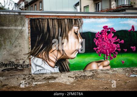 Ein Graffiti an einer alten Mauer zeigt ein Mädchen, welches wie bei einer Pusteblume ein Coronavirus anpustet, welches dann auseinander fliegt. Ein s Stockfoto