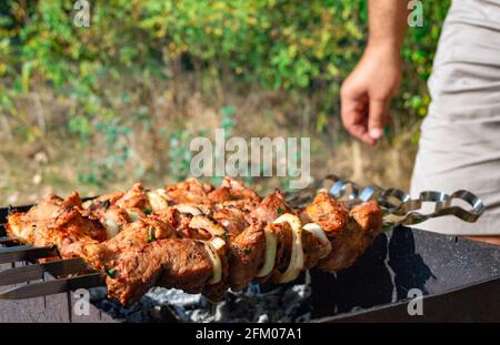 Mann, der Fleisch auf Metallspießen kocht. Grillen Sie im Freien. Picknick am Wochenende. Stockfoto