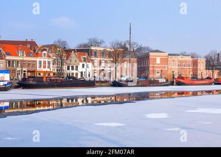 Traditionelle Häuser und Boote, die im gefrorenen Kanal des Flusses Spaarne, Haarlem, Amsterdam, Nordholland, Niederlande, festgemacht sind Stockfoto