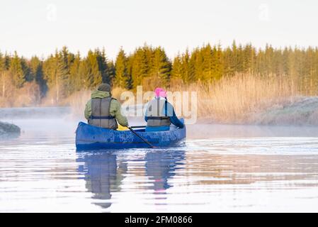 Rentner rudern im frühen Frühjahr am frühen Morgen ein Kanu. senioren Lebensstil. Morgenlandschaft, Nebel am Morgenfluss und Menschen im Kanu Stockfoto