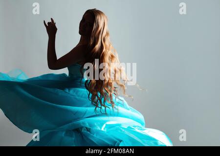 Geheimnisvolle junge Frau mit langen welligen Haaren und einem üppigen blauen Kleid. Prinzessin im Schatten, ein fabelhaftes Bild. Stockfoto