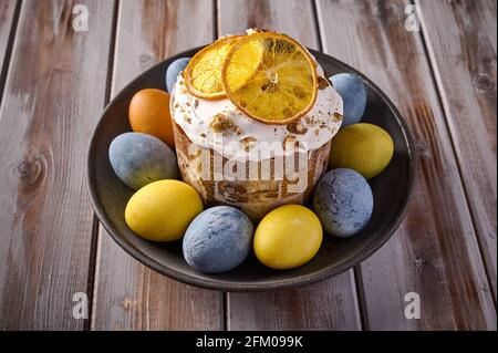 Hausgemachter Osterkuchen und bunt bemalte Eier auf schwarzem Teller vor einem Hintergrund aus strukturierten Brettern. Nahaufnahme Stockfoto