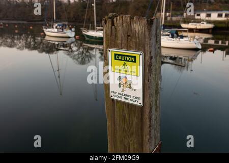 Vorsicht Stolpergefahr, achten Sie auf Ihren Schritt, Schild am Kai in Caernarfon, Wales. Mit Marina im Hintergrund Stockfoto