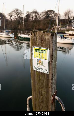 Vorsicht Stolpergefahr, achten Sie auf Ihren Schritt, Schild am Kai in Caernarfon, Wales. Mit Marina im Hintergrund Stockfoto