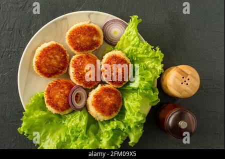 Juicy Delicious mit Paniermehl und gebratenen Hähnchenschnitzel auf weißem Teller mit Gewürzen in Holzschüttlern auf dunklem Hintergrund überzogen, Blick von oben. Stockfoto