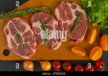 Rohe Schweinebraten - bereit zum Kochen mit Kräutern und Tomaten. Holzhintergrund. Stockfoto