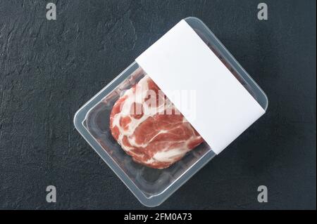 Rohes marmoriertes Schweinesteak in Vakuumverpackung auf schwarzem Hintergrund, Draufsicht, Logo-Mockup für Design. Stockfoto