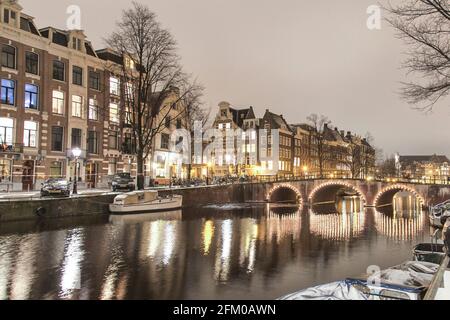Traditionelle Häuser und Brücke entlang des beleuchteten Keizersgracht-Kanals bei Nacht, Amsterdam, Nordholland, Niederlande Stockfoto
