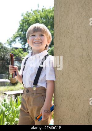 Fröhlich niedlichen Jungen 5-6 Jahre alt ist die Vorbereitung für die Schule. Steht an einem sonnigen Tag im Freien in einem weißen Hemd und hält bunte Filzstifte in seinem han Stockfoto