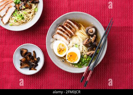 Ramen-Nudeln mit Schweinefleisch und Ei in Schüssel auf rotem Textilhintergrund, Draufsicht Stockfoto