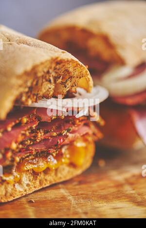 Dünn geschnittener Pastrami-Sand, der sich mit köstlichen Speisen auf Baguette-Brot mit Käsekäse, Zwiebeln trifft Stockfoto