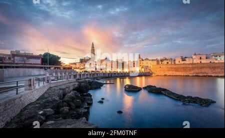 Monopoli Hafen in der Metropolstadt Bari und Region Apulien (Apulien), Italien bei Sonnenuntergang und schöne beleuchtete Kathedrale Stockfoto