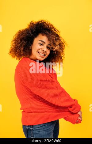 Fröhliche junge schwarze Frau lächelt und schaut in einem Studio vor gelbem Hintergrund auf die Kamera. Stockfoto