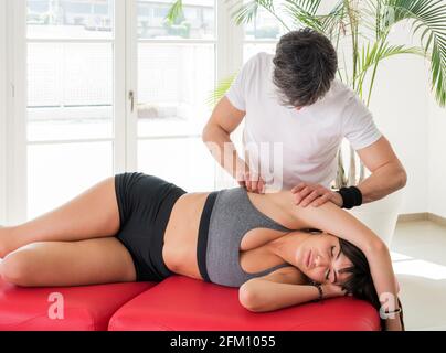 Männlicher Osteopath, der eine Triggerpunktbehandlung bei einer jungen Frau durchführt Druck mit den Fingern ausüben, um die Spannung zu lösen und zu entlasten Schmerzen Stockfoto