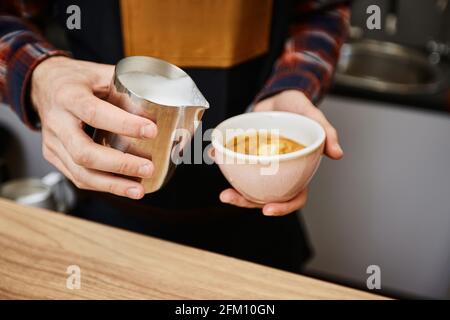 Kaukasischer Mann, der heiße Milch in Kaffee gießt. Stockfoto