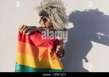 Lockige spanische süße Frau mit einer Tragetasche mit einer Flagge Und Tattoos auf weißem Wandhintergrund Stockfoto