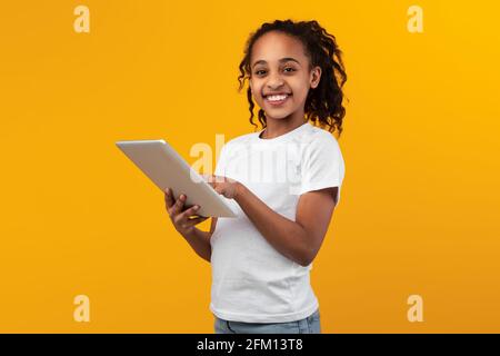 Schwarzes Mädchen steht mit Tablet im gelben Studio Stockfoto