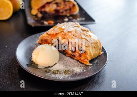 Köstlicher frischer Strudel gefüllt mit Äpfeln und Rosinen, serviert mit einer Kugel Eis, schönes Dessert, schwarzer Hintergrund. Stockfoto