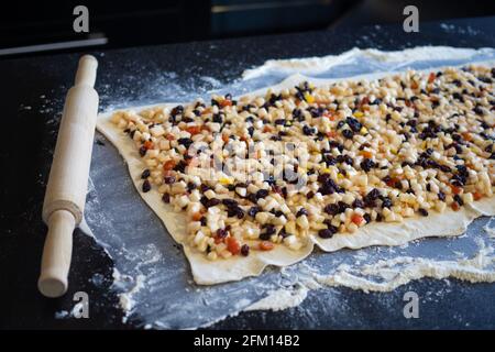 Prozess der Herstellung von Apfelstrudel, eine Schicht Teig mit der Füllung auf dem Tisch gelegt, ist der Strudel bereit, verdreht und in den Ofen geschickt werden. Stockfoto