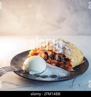 Köstlicher frischer Strudel gefüllt mit Äpfeln und Rosinen, serviert mit einer Kugel Eis, schönes Dessert, grauer Hintergrund. Stockfoto