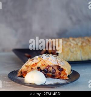 Köstlicher frischer Strudel gefüllt mit Äpfeln und Rosinen, serviert mit einer Kugel Eis, schönes Dessert, grauer Hintergrund. Stockfoto