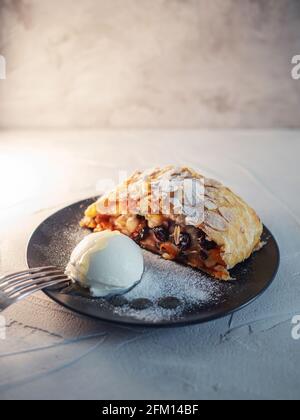 Köstlicher frischer Strudel gefüllt mit Äpfeln und Rosinen, serviert mit einer Kugel Eis, schönes Dessert, grauer Hintergrund. Stockfoto