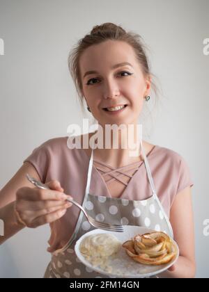 Die glückliche Köchin hält einen Teller mit Apfelrosen bereit, der von ihr selbst zubereitet wird. Stockfoto