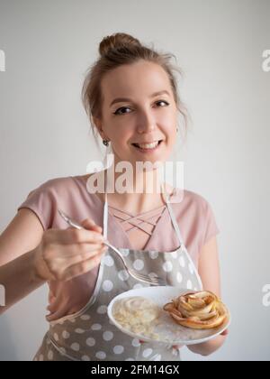 Die glückliche Köchin hält auf der Schürze einen Teller mit Apfelrosen, der von ihr selbst zubereitet wird. Stockfoto