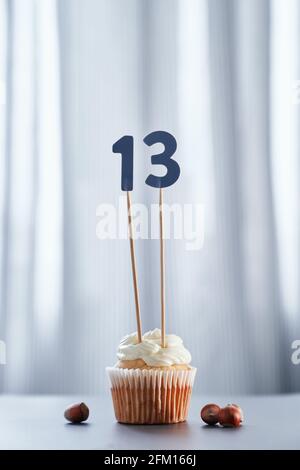 Geburtstagskuchen oder Muffin mit der Nummer 13 dreizehn und Haselnüssen auf dem Tisch und hellem Hintergrund. Geburtstag oder Jubiläum Grußkarte Konzept. Hochwertige vertikale Fotos Stockfoto
