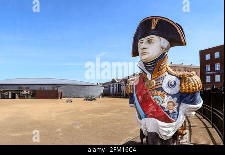 HMS Trafalgar Galionsfigur des Vizeadmiral Horatio Lord Nelson mit dem Mary Rose Museum im Hintergrund, Portsmouth Historic Dockyard, Portsmouth. Stockfoto