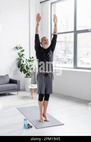 Die ganze Länge der bärtigen und tätowierten Mann trainieren auf Fitness Matte in der Nähe von Kurzhanteln im Wohnzimmer Stockfoto