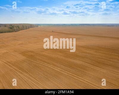 Der rote Traktor pflügt, bebaut an einem Frühlingstag ein riesiges Feld mit blauem Himmel. Foto mit einer Drohne Stockfoto