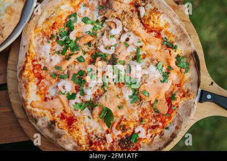 Pescatore Pizza mit Lachs Thunfisch Garnelen Mozzarella auf einem hölzernen Rundes Tablett Stockfoto