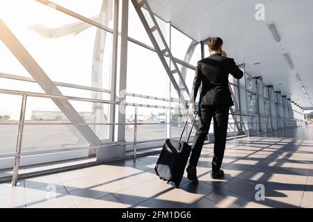 Geschäftsmann in Anzug, der mit Koffer am Flughafen vorbei läuft, Rückansicht Stockfoto