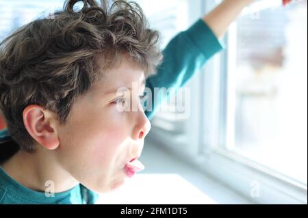 Niedliche kleine Junge Grimassen am offenen Fenster und Sticks Aus der Zunge Stockfoto