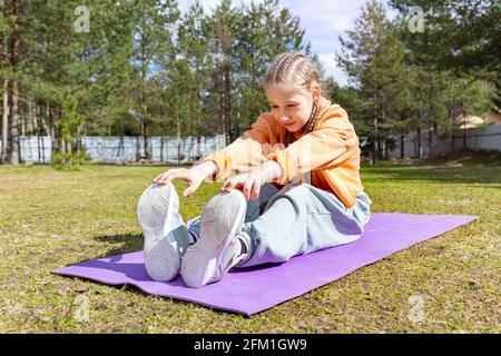 Teenager-Mädchen tun Stretching-Übungen, während auf einem Sport sitzen Matte im Freien Stockfoto