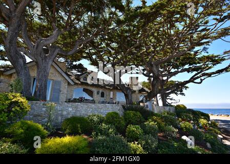 Außenansicht eines aus Stein erbauten Luxushauses, umgeben von Zypressen und einem glitzernden tropischen Garten in Carmel-by-the-Sea, Kalifornien, USA. Stockfoto