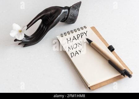 Happy Monday Word in offenem Notizbuch und Blume in schwarzer Hand. White Office Workplace Stockfoto