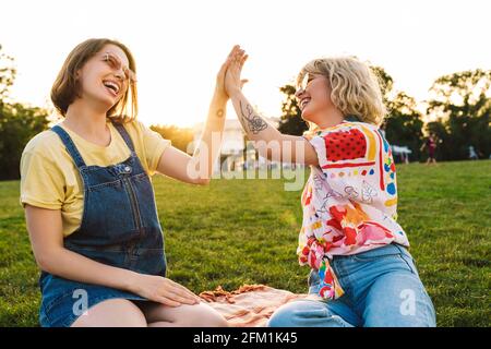 Bild von lustigen zwei Frauen in Sonnenbrillen lachen und geben Hoch fünf während der Erholung im Sommerpark Stockfoto