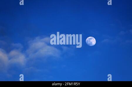 Langsam still, der frühe Abendmond an einem tiefblauen Himmel mit hellen Wolken gesehen Stockfoto